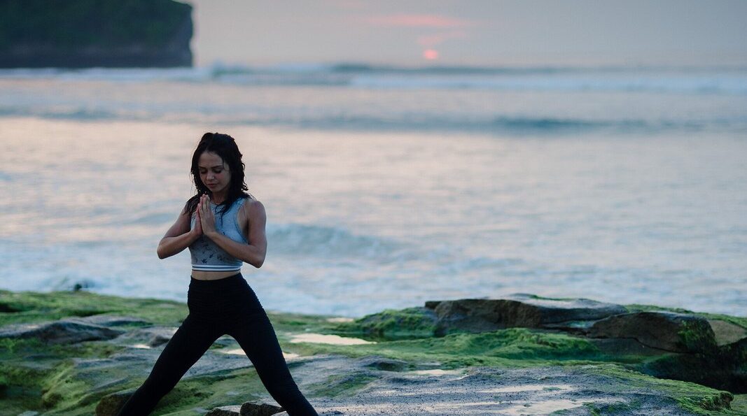 Sesión de yoga frente al mar al amanecer, sobre las rocas de la orilla