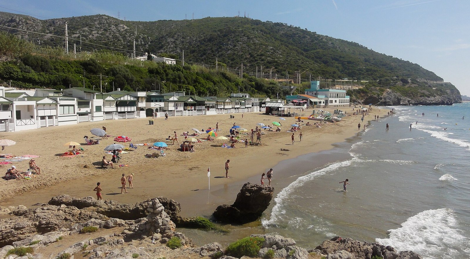 Garraf beach with its white bathing huts and the green hills of the Garraf massif, next to Sitges